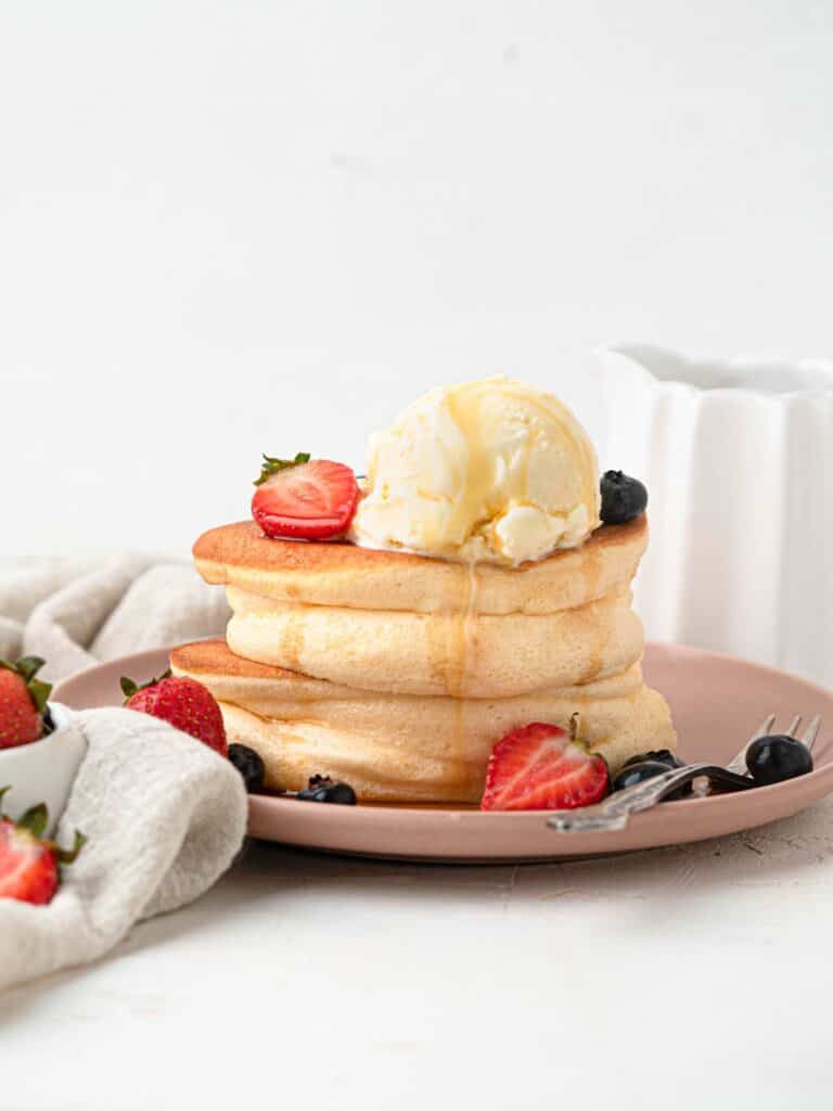 Thick Fluffy Japanese style souffle pancakes with ice cream, berries and maple syrup