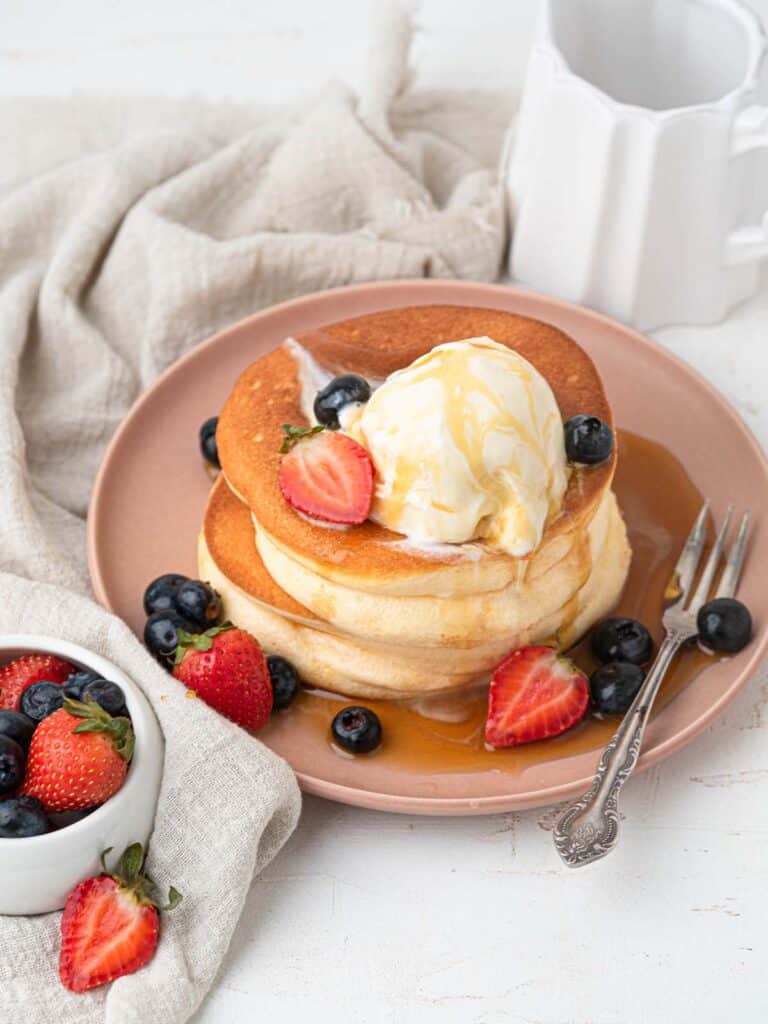 Thick Fluffy Japanese style souffle pancakes with ice cream, berries and maple syrup