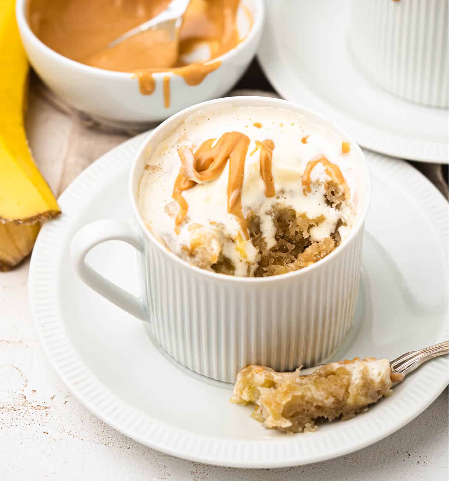 banana bread mug cake topped with whipped cream and peanut butter