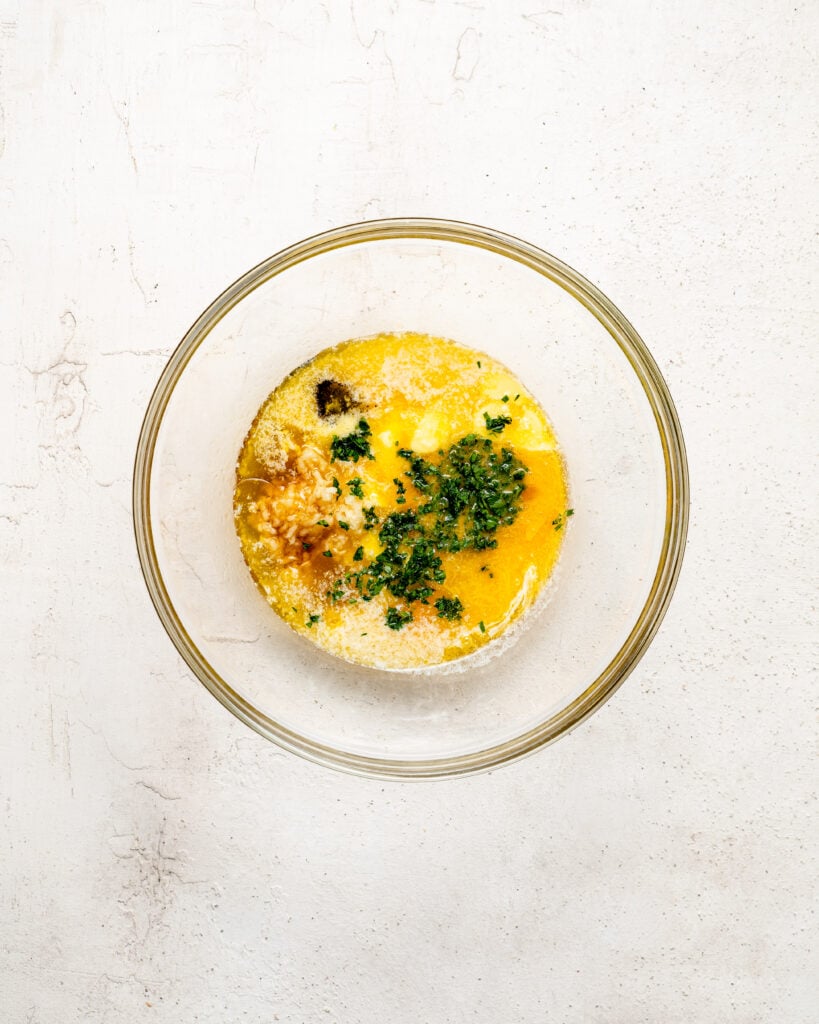 Yellow garlic butter mixture with green herbs and minced pieces in a glass bowl - Catherine Zhang Yellow garlic butter mixture with green herbs and minced pieces in a glass bowl