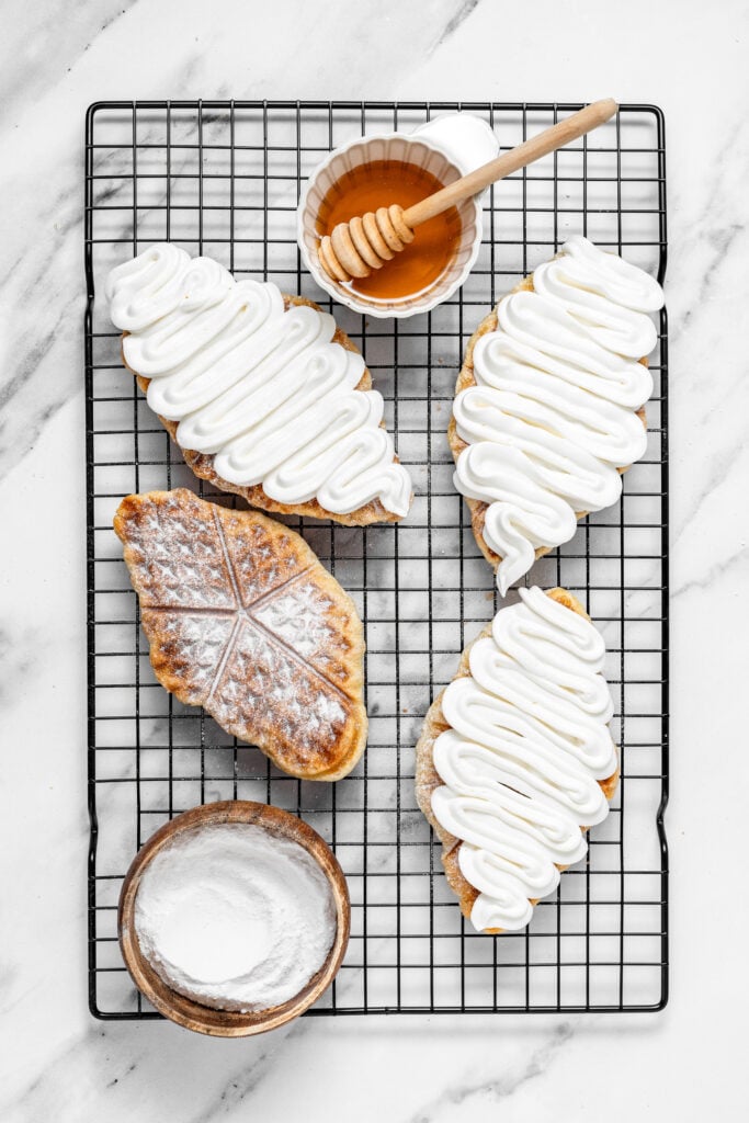 Croffles on a wire rack topped with piped whipped cream and dusted powdered sugar - Catherine Zhang Croffles on a wire rack topped with piped whipped cream and dusted powdered sugar