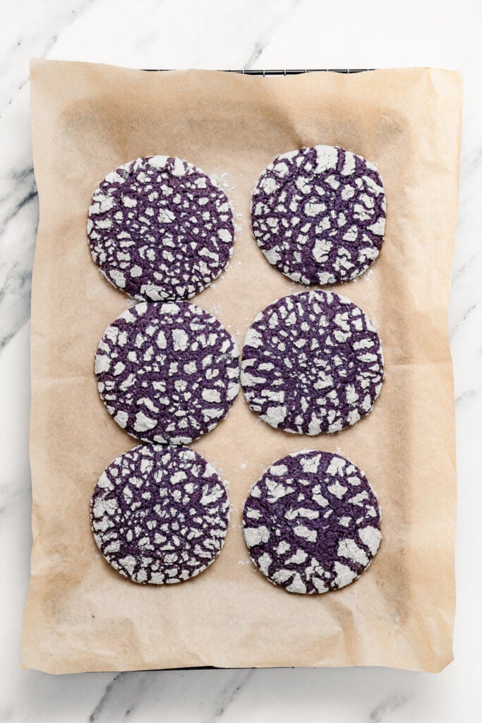Finished Ube Crinkle Cookies with white cracked tops on parchment paper - Catherine Zhang Finished Ube Crinkle Cookies with white cracked tops on parchment paper