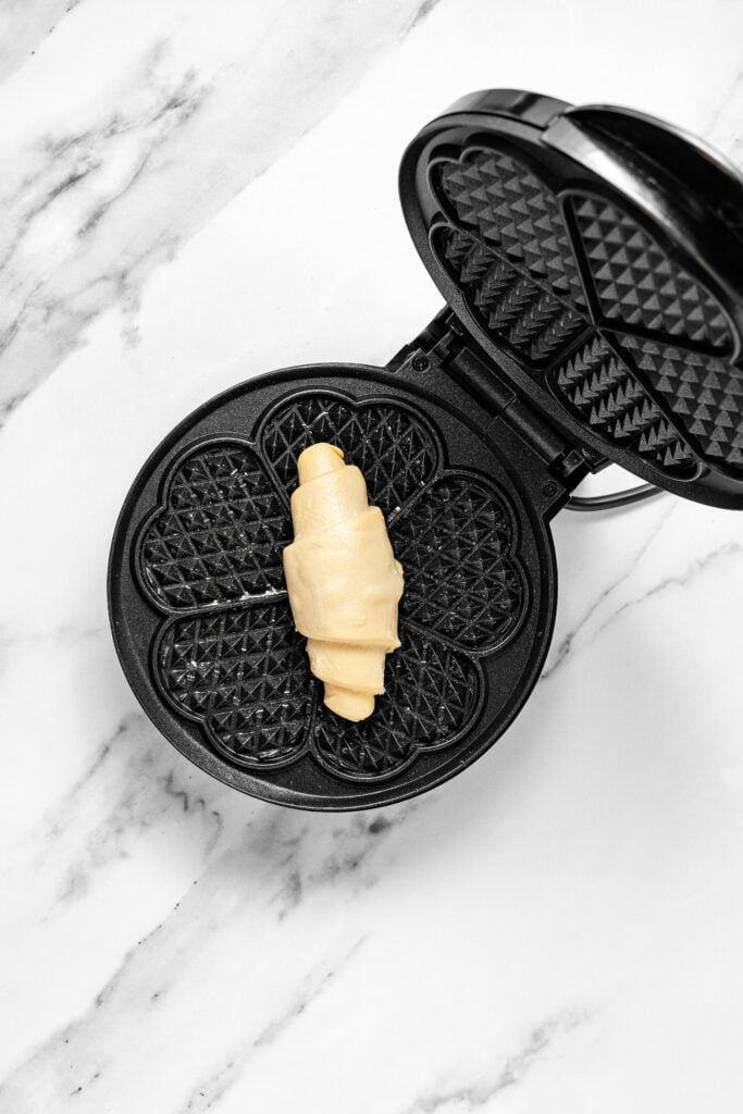 Folded pale dough piece placed inside a waffle iron for croffles - Catherine Zhang Folded pale dough piece placed inside a waffle iron for croffles