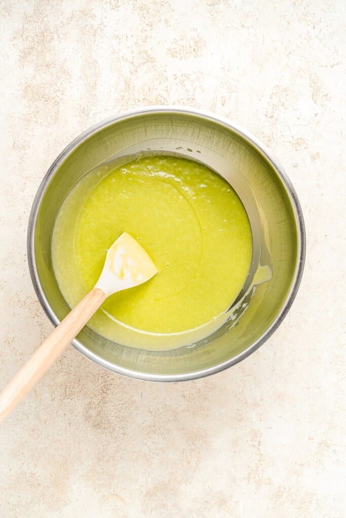 Green liquid in a metal bowl - Catherine Zhang Top-down view of a silky green sauce being mixed in a stainless steel bowl with a wooden spatula inside the bowl.