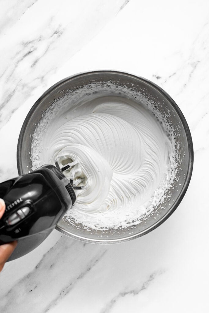 Hand mixer whipping thick white cream in a metal bowl for croffles - Catherine Zhang Hand mixer whipping thick white cream in a metal bowl for croffles