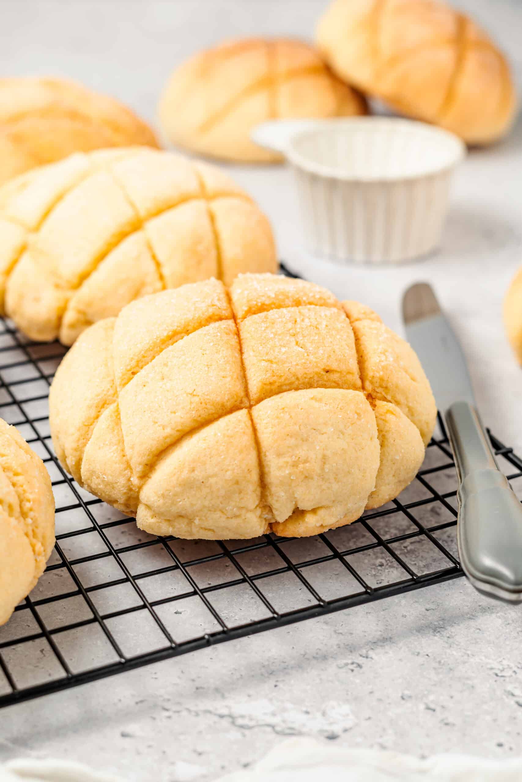 Golden round dinner rolls with cross cuts cooling on a wire rack, with baking tools in the background