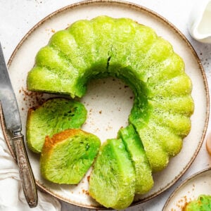Bright green pandan bundt cake ring on a plate, sliced to reveal a fluffy interior.