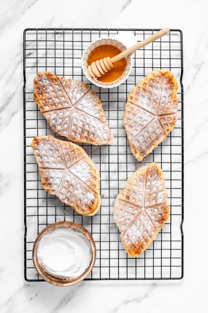 Powdered sugar dusted croffles cooling on a black wire rack - Catherine Zhang Powdered sugar dusted croffles cooling on a black wire rack