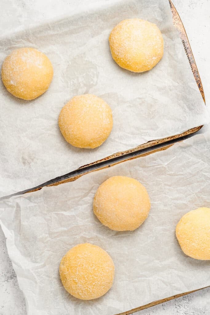 Rounded Melon Pan dough pieces with coated yellow surfaces on parchment
