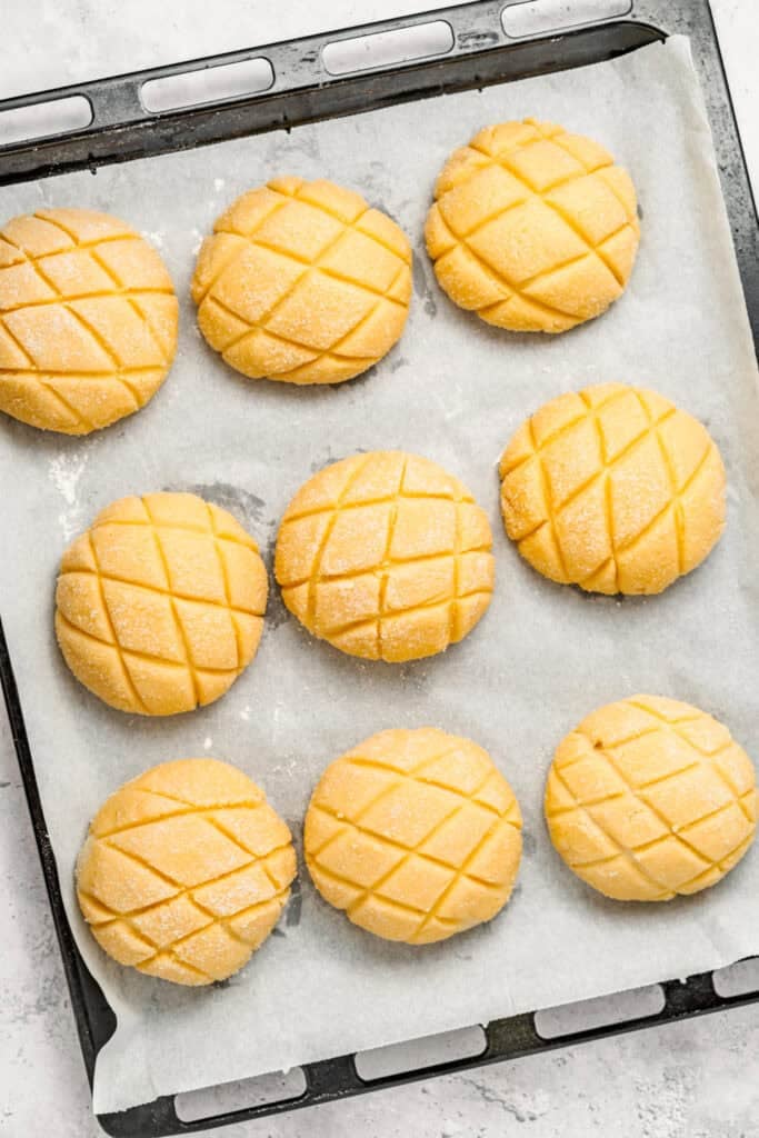 Scored Melon Pan buns spaced on a parchment-lined baking tray