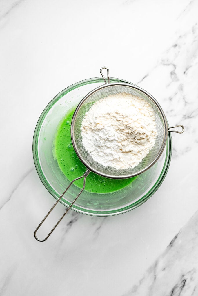 Sifting flour into green pandan egg yolk mixture for pandan chiffon cake - Catherine Zhang Sifting flour into green pandan egg yolk mixture for pandan chiffon cake