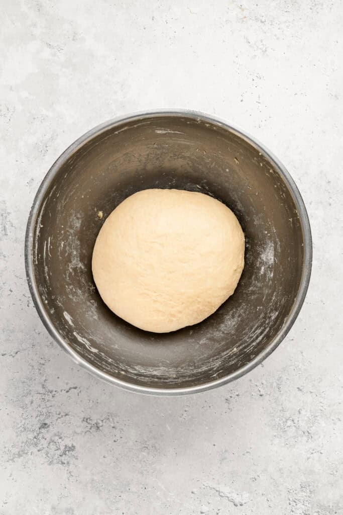 Dough ball resting in a stainless steel mixing bowl on a light gray countertop