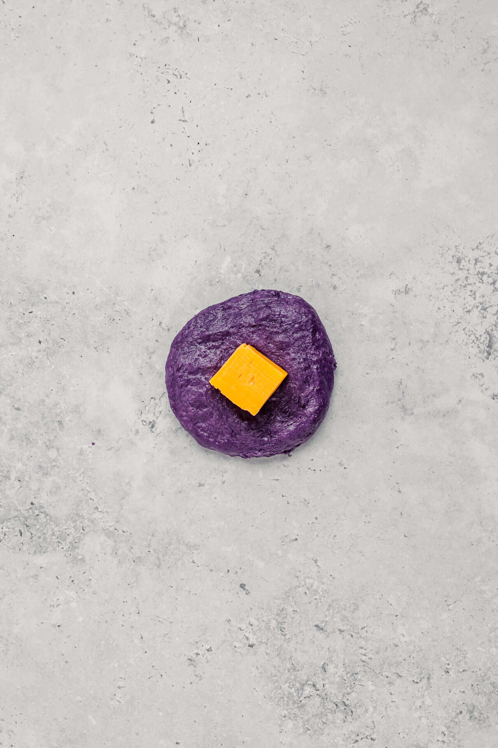 Stuffing Cheese Into Ube Pandesal - Catherine Zhang Cube of cheddar placed in the center of a flattened ube pandesal dough disc