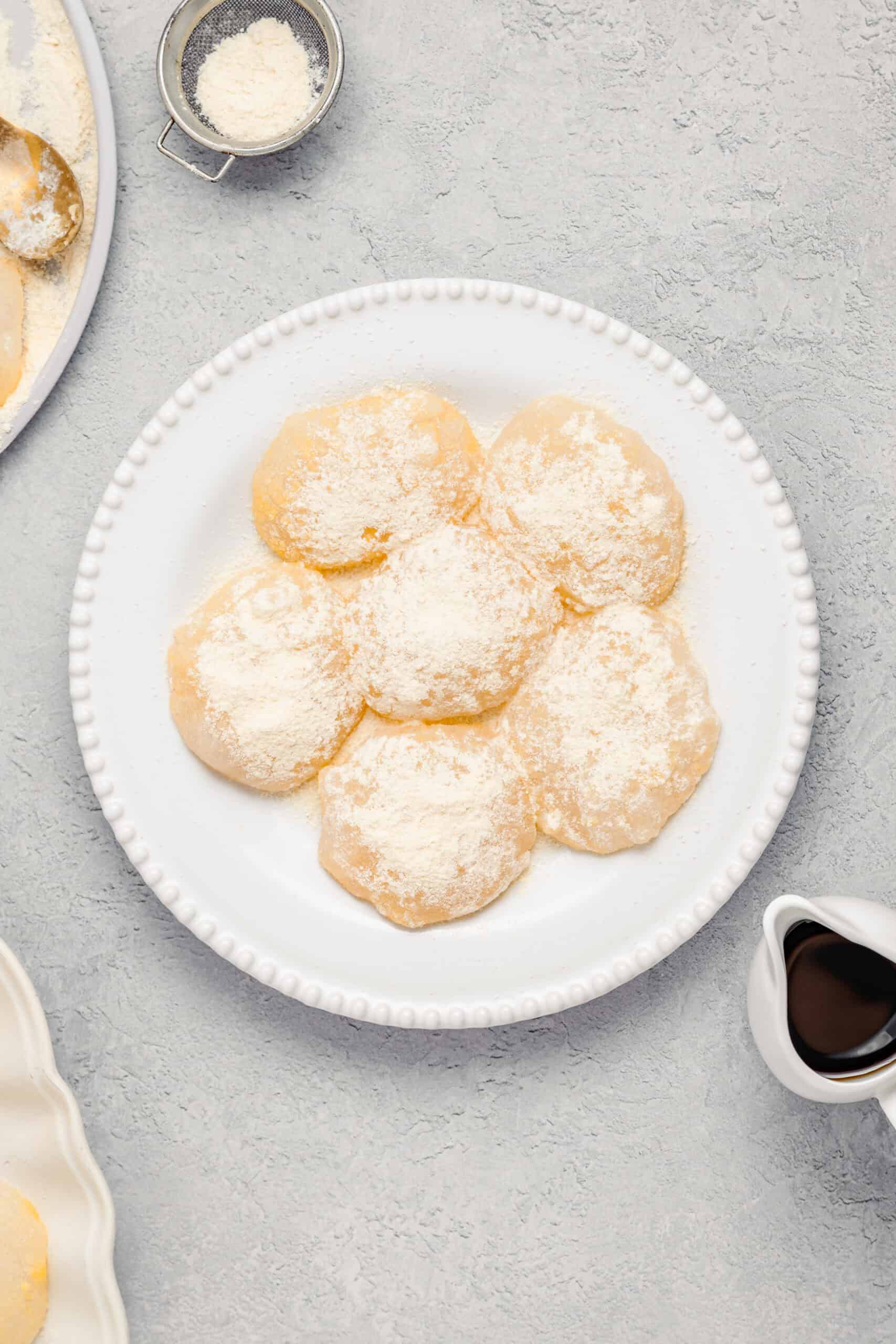 Soft warabimochi pieces coated in kinako on a scalloped white plate - Catherine Zhang Soft warabimochi pieces coated in kinako on a scalloped white plate