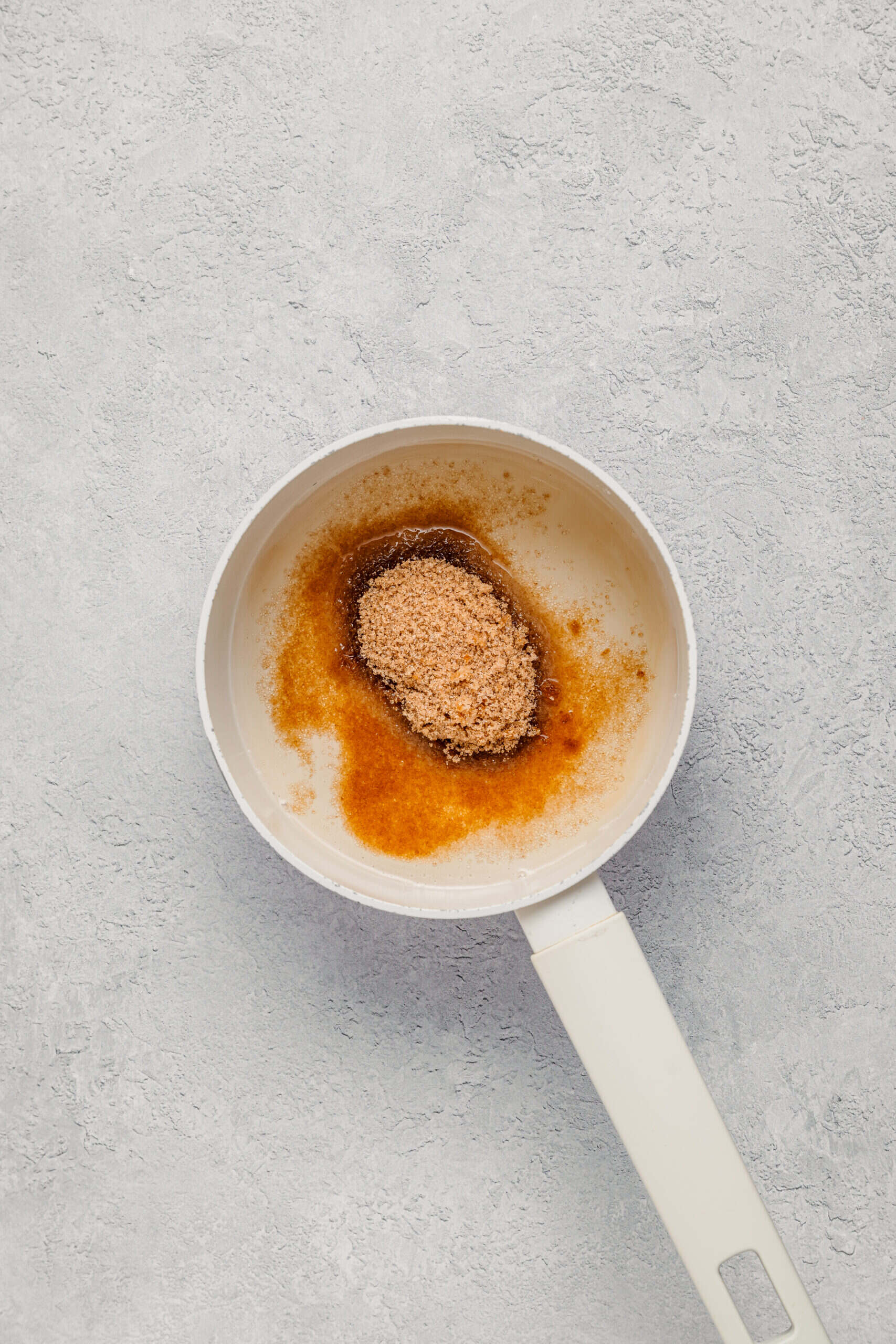 Japanese black sugar and water in a small saucepan for kuromitsu syrup - Catherine Zhang Japanese black sugar and water in a small saucepan starting to dissolve into kuromitsu