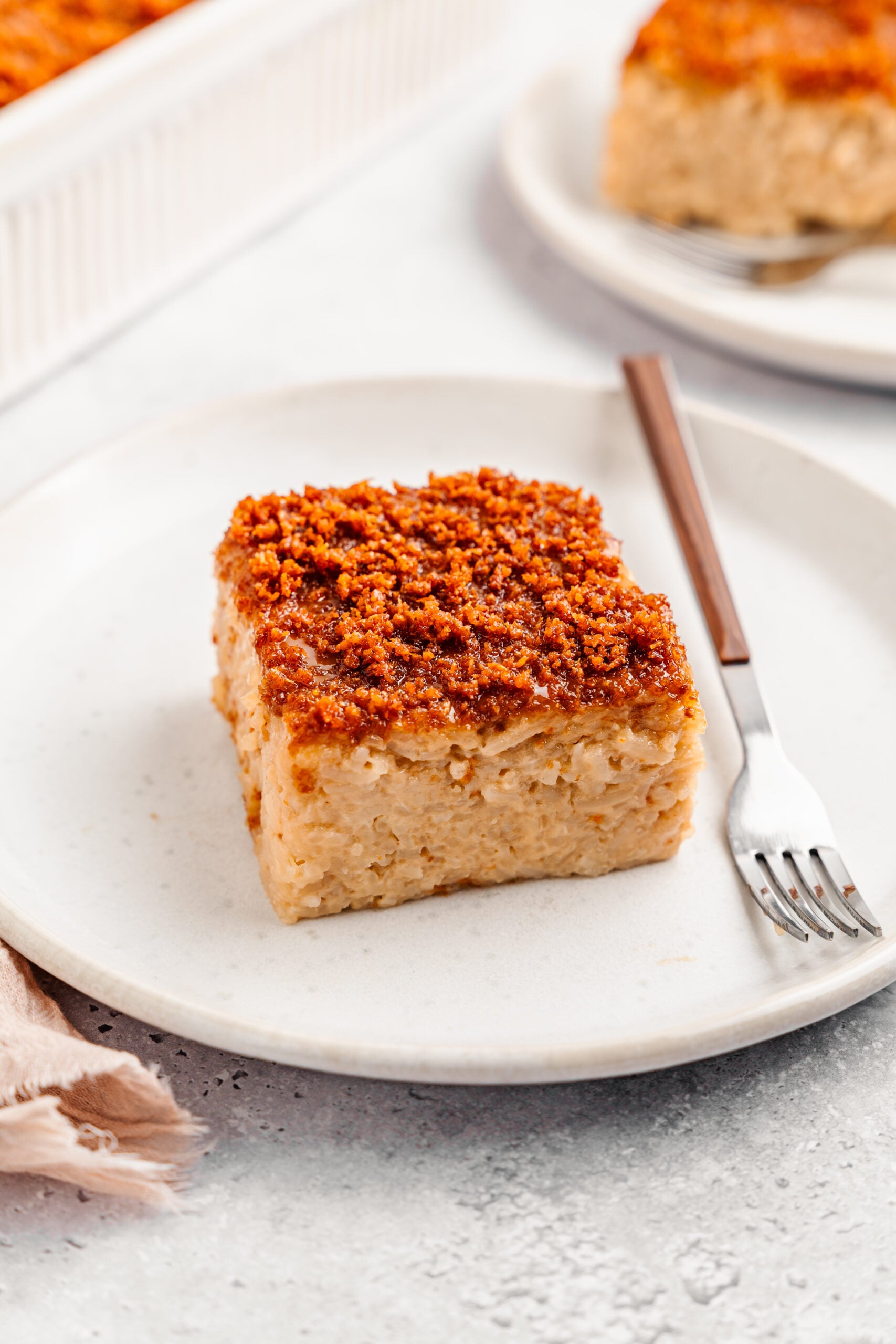 Square of Filipino biko sticky rice cake on a white plate topped with crisp golden latik - Catherine Zhang Square of Filipino biko sticky rice cake on a white plate topped with crisp golden latik