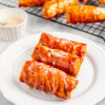 Three crispy turon Filipino banana lumpia on a white plate with condensed milk and flaky salt