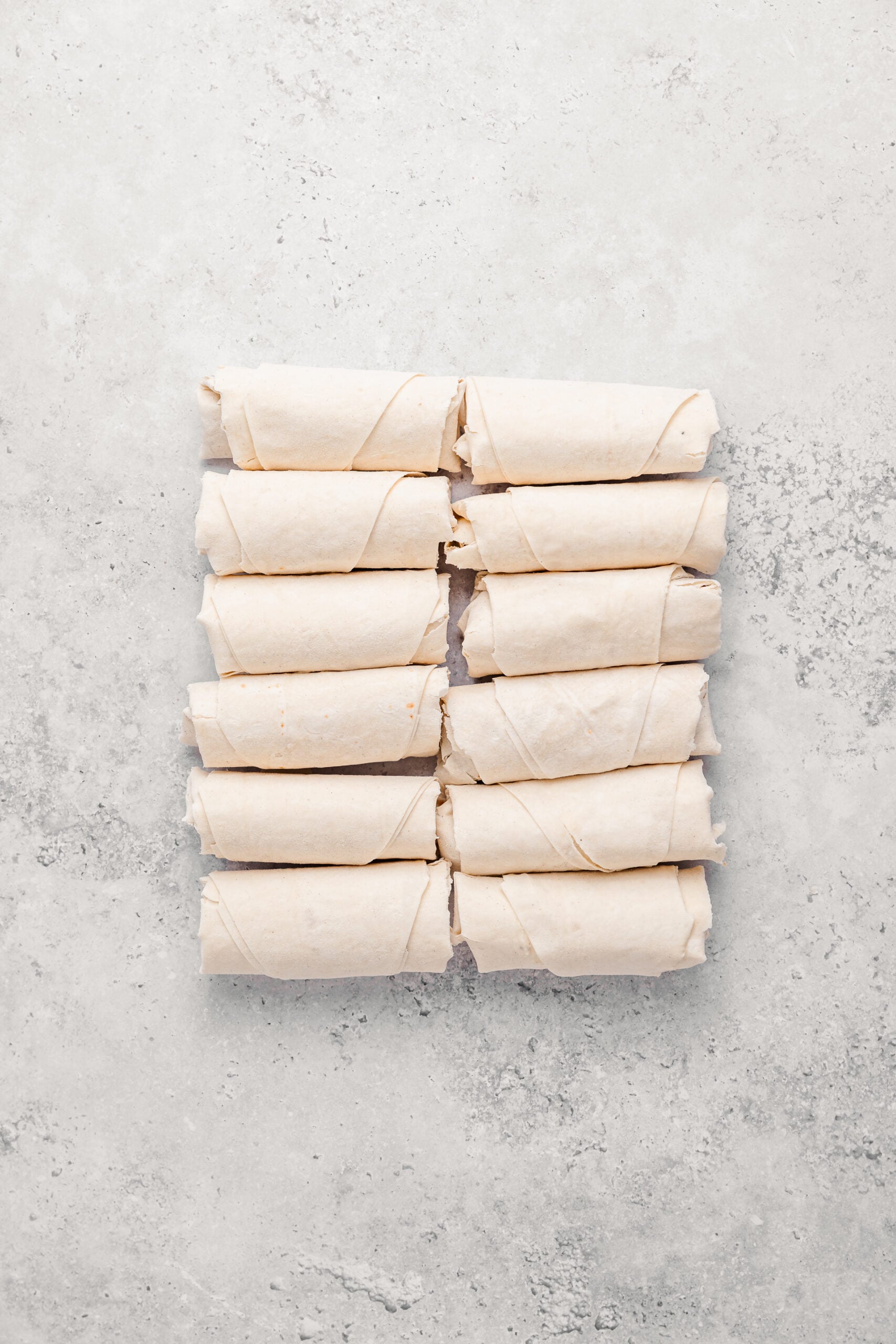 Twelve rolled and sealed turon parcels lined up before frying - Catherine Zhang Twelve rolled and sealed turon parcels lined up before frying