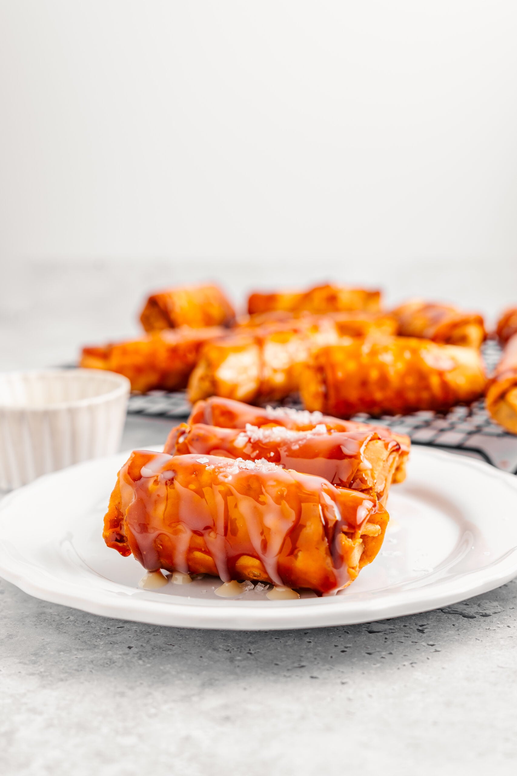 A single crispy turon on a white plate with condensed milk drizzle - Catherine Zhang A single crispy turon on a white plate with condensed milk drizzle