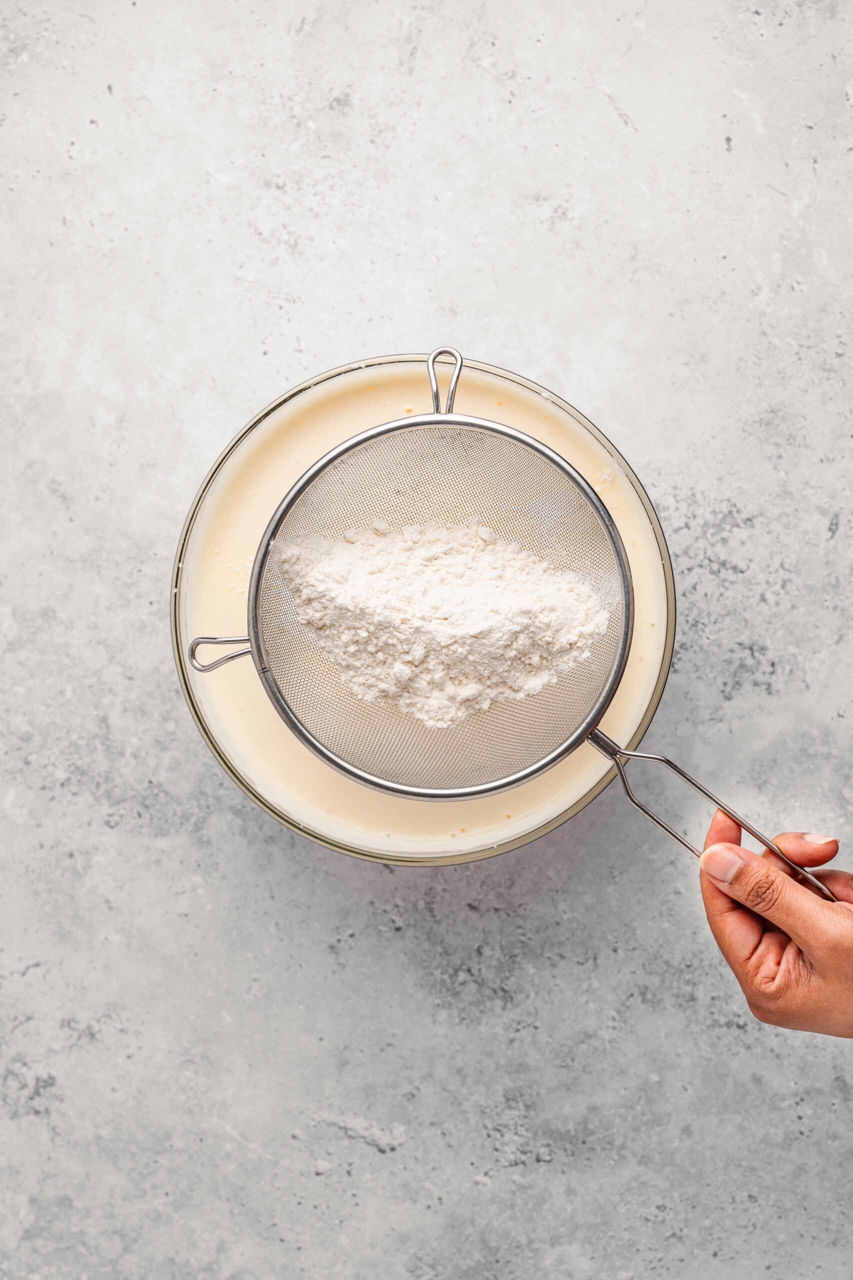 Sifting bread flour through a sieve over Japanese castella cake batter - Catherine Zhang Sifting bread flour through a sieve over Japanese castella cake batter
