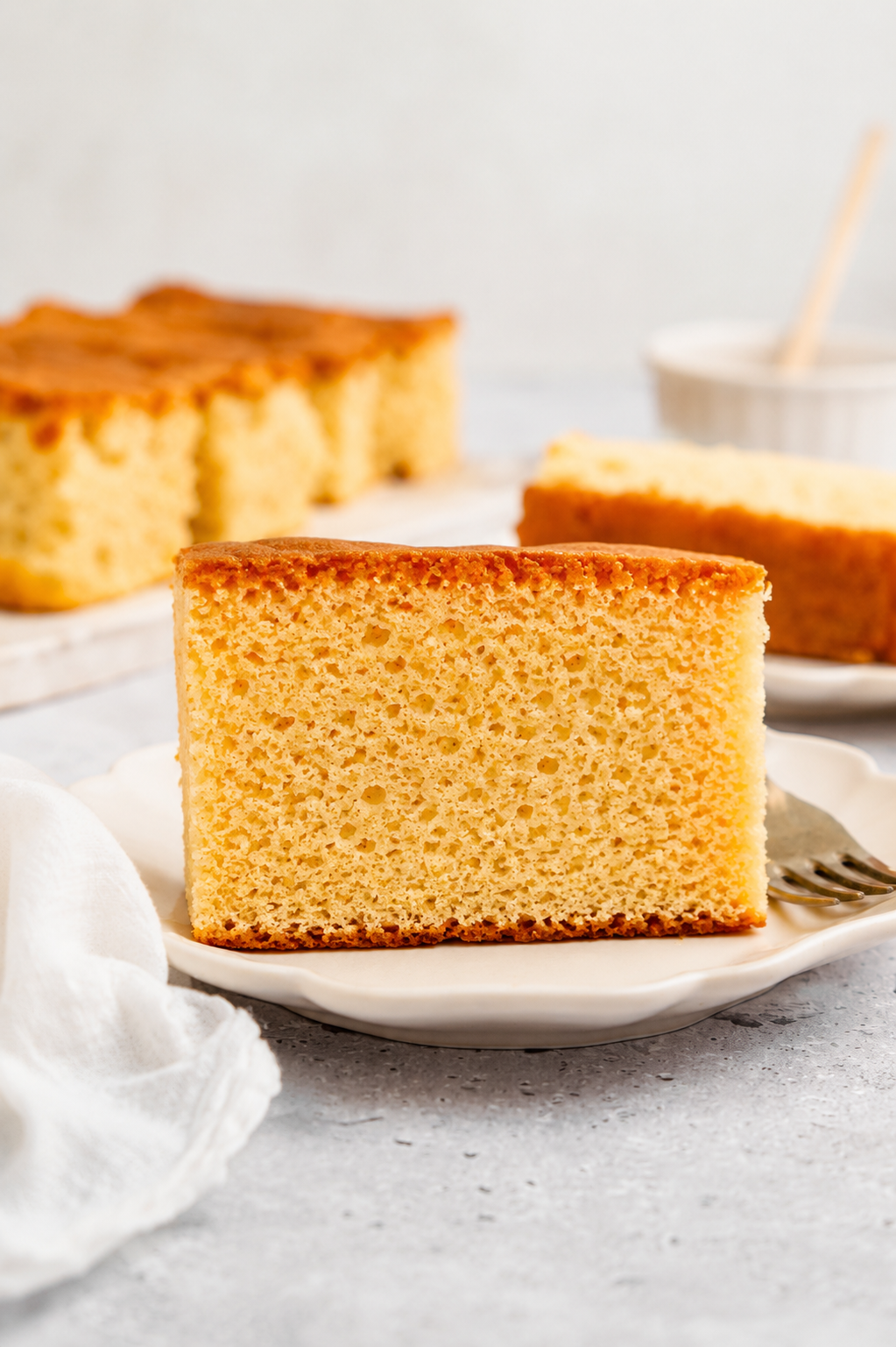 Slice of Japanese castella cake on a white plate showing the fine moist crumb - Catherine Zhang Slice of Japanese castella cake on a white plate showing the fine moist crumb