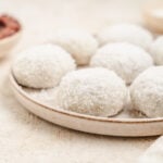 Red bean mochi on a ceramic plate with a bowl of red bean paste behind