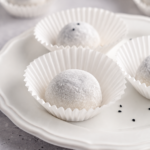 Black sesame mochi dusted with starch in paper cases on a white plate