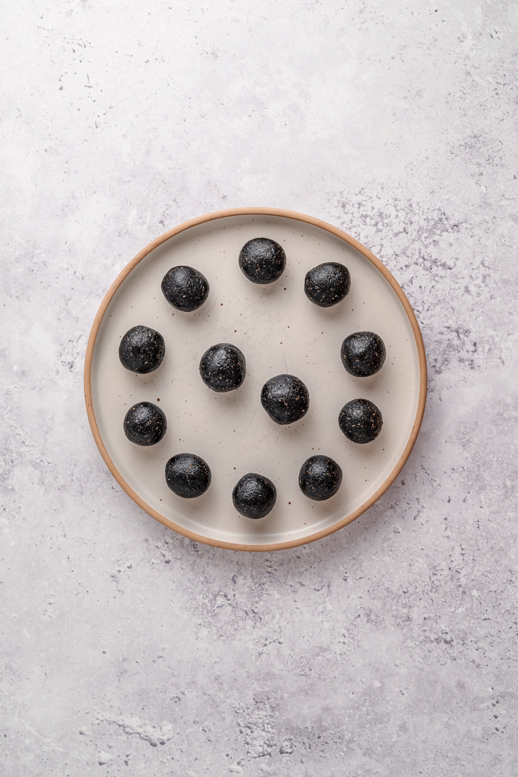 Rolled black sesame filling balls - Catherine Zhang Twelve rolled balls of black sesame filling on a plate ready for the freezer