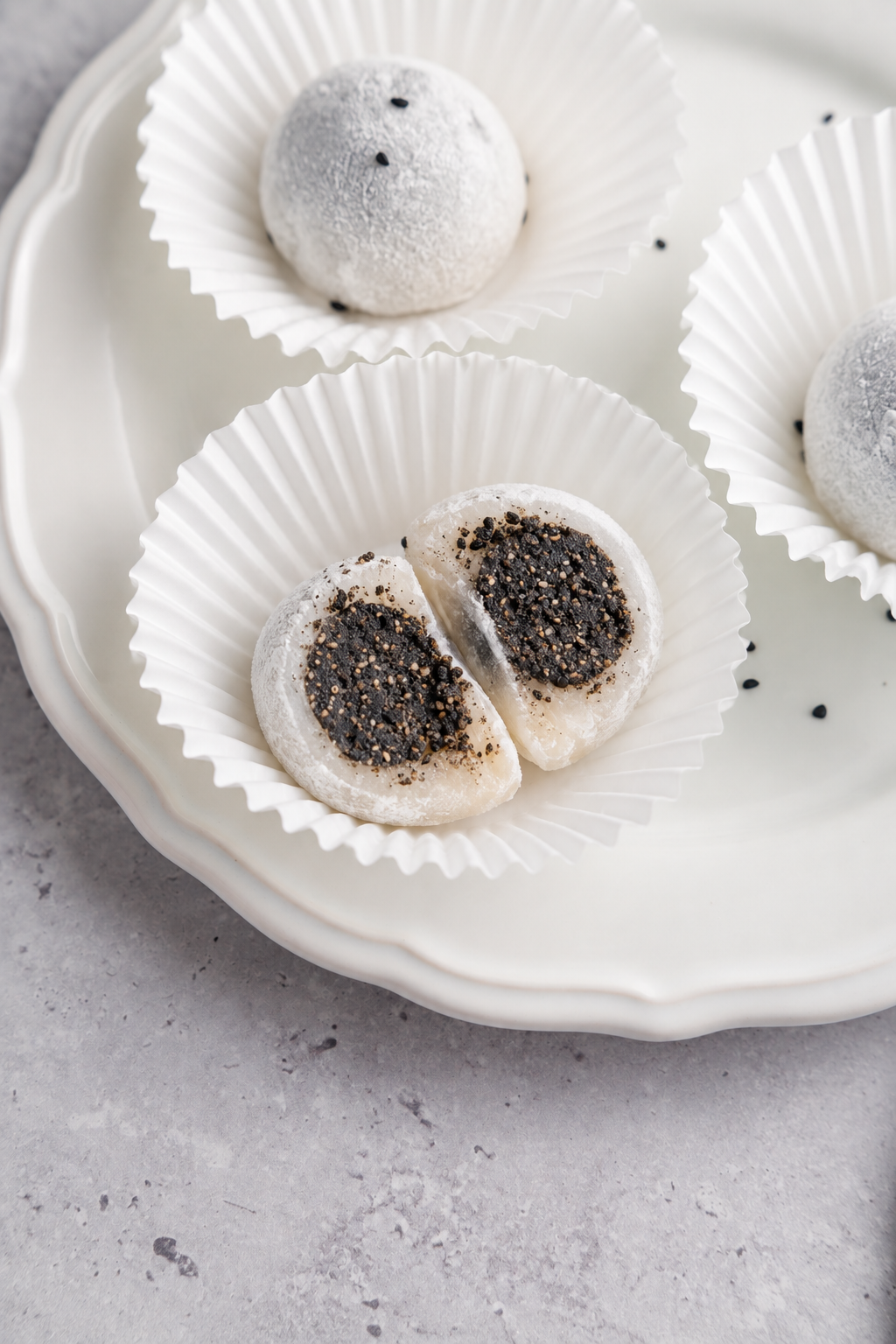 Black sesame mochi filling - Catherine Zhang Halved black sesame mochi on a plate beside a whole dusted round
