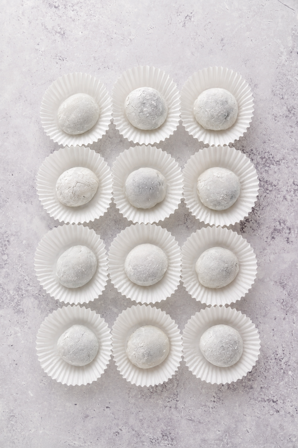 Finished black sesame mochi - Catherine Zhang Twelve finished black sesame mochi sitting in white paper cases