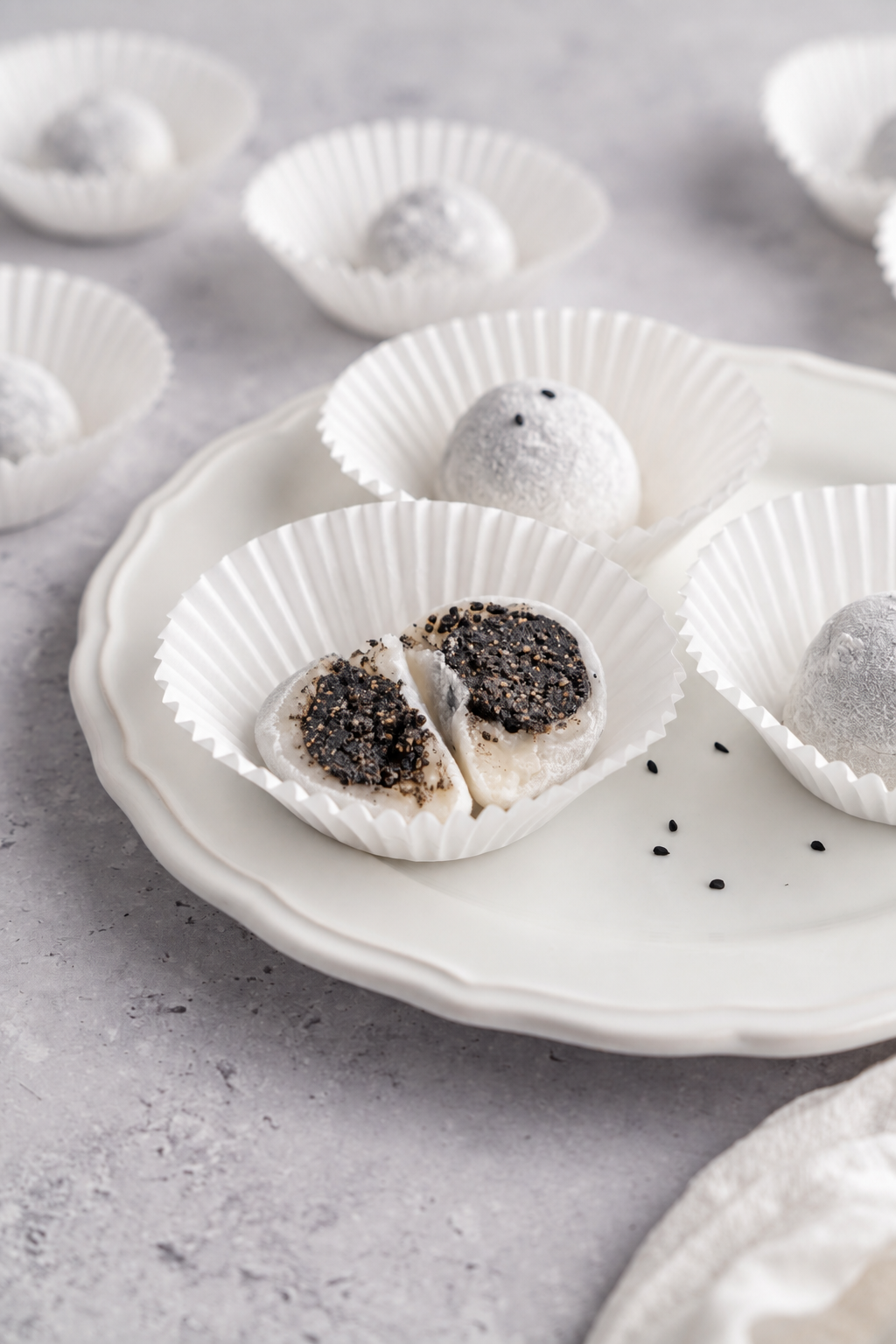 Black sesame mochi served - Catherine Zhang Black sesame mochi served on a white plate with scattered sesame seeds