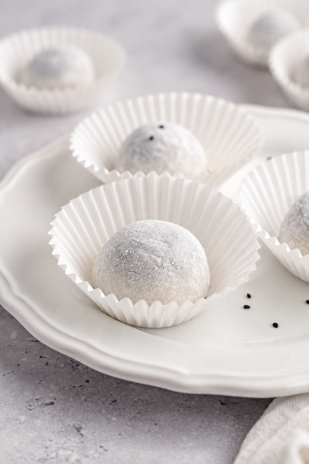 Black sesame mochi - Catherine Zhang Black sesame mochi dusted with starch in paper cases on a white plate