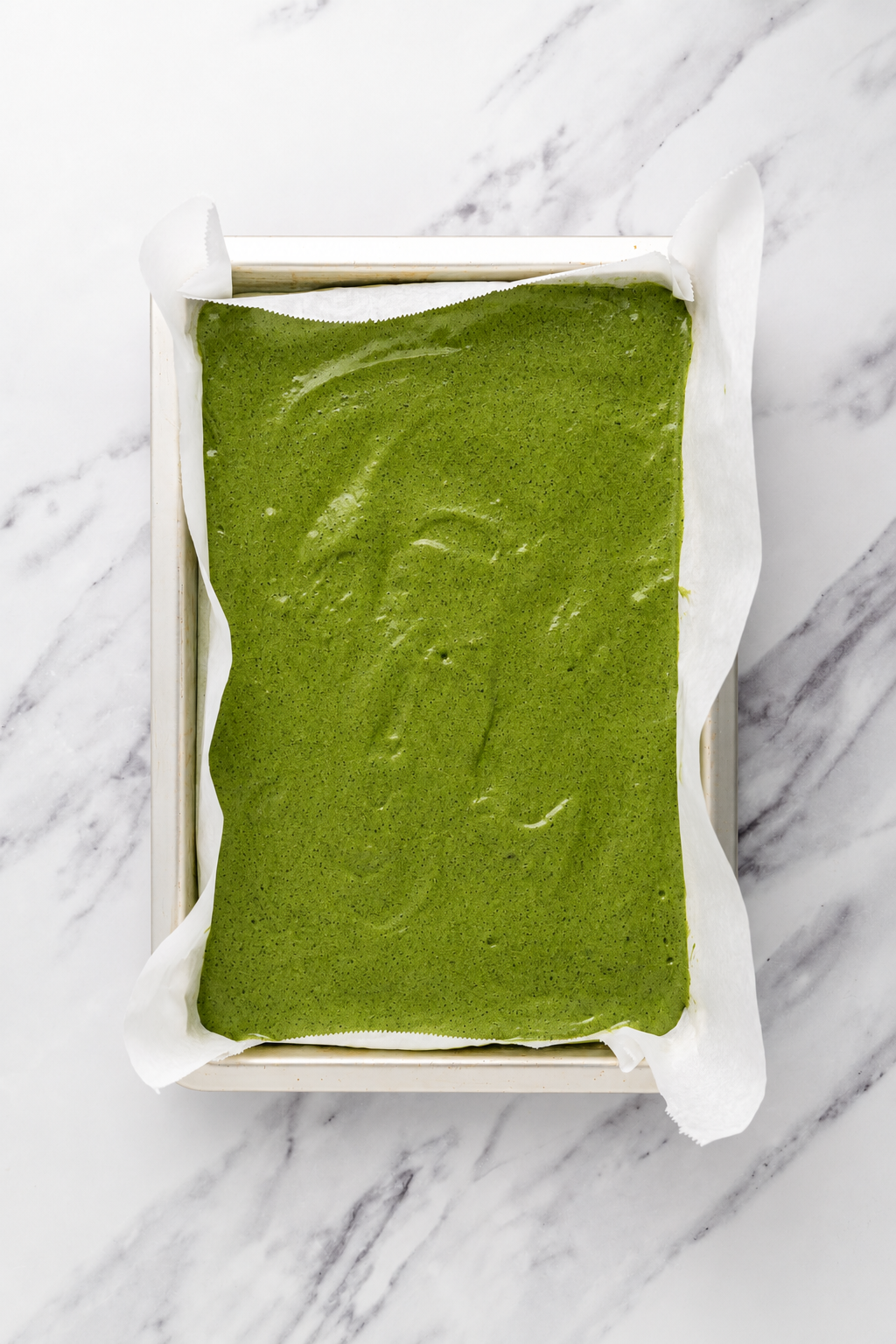 Matcha batter in the pan - Catherine Zhang Matcha sponge batter spread level in a parchment lined pan