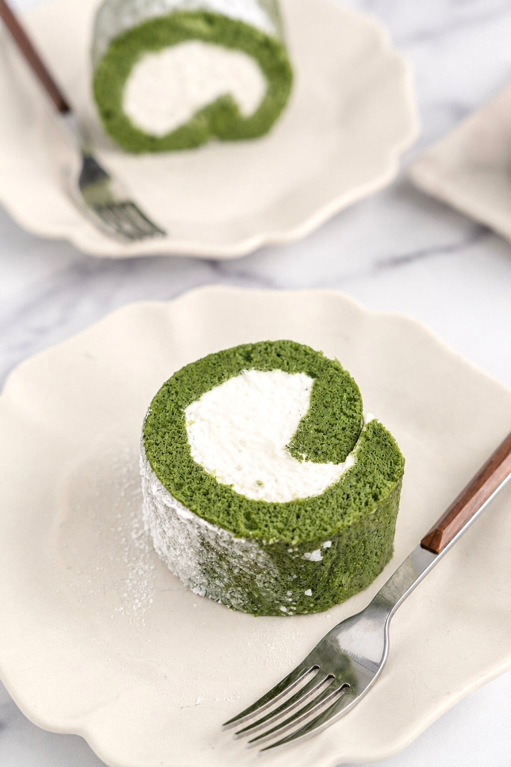 Matcha roll cake served - Catherine Zhang Matcha roll cake served on a scalloped plate with a fork