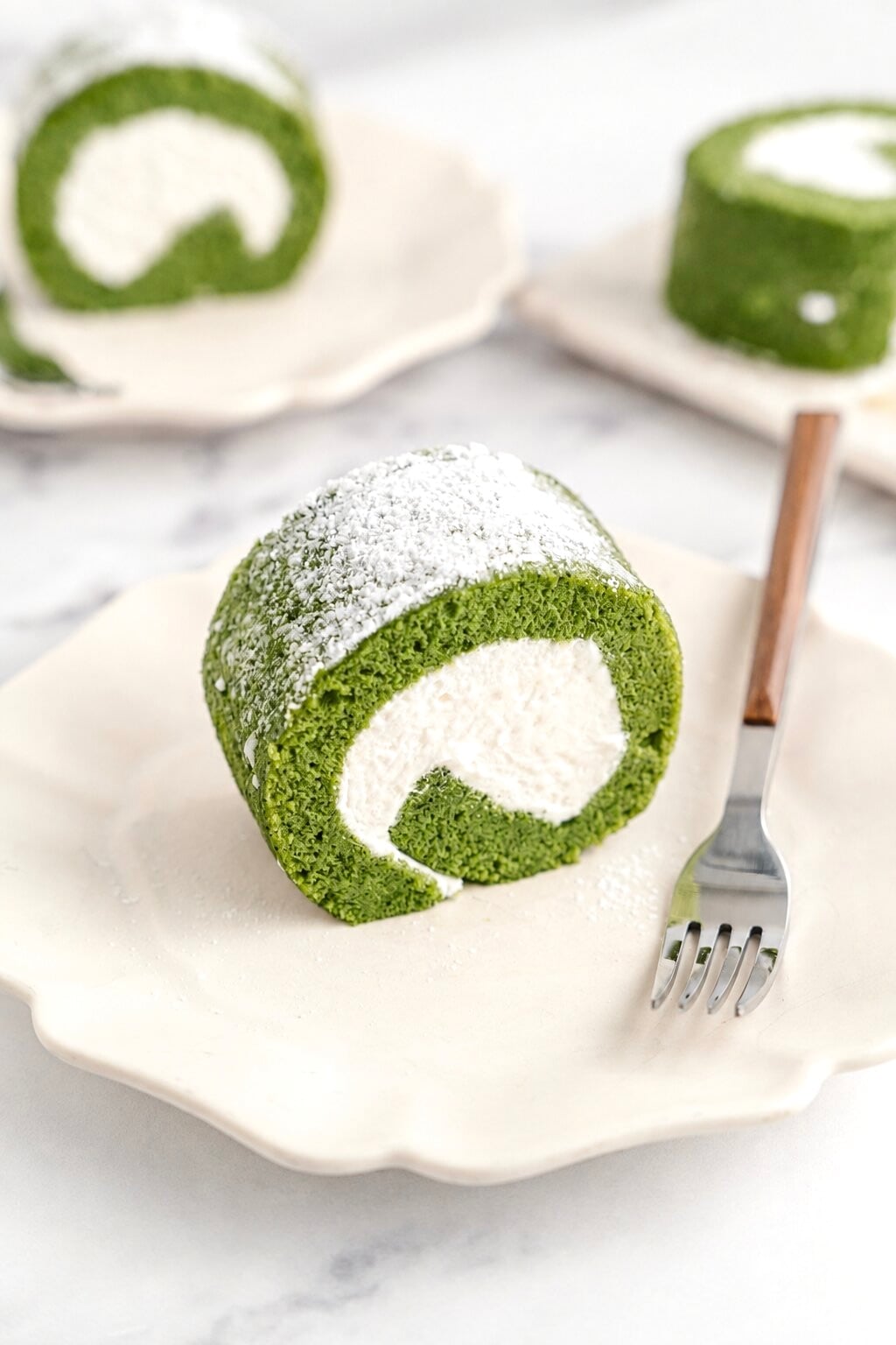 Matcha roll cake slice - Catherine Zhang A slice of matcha roll cake on a white plate with a fork