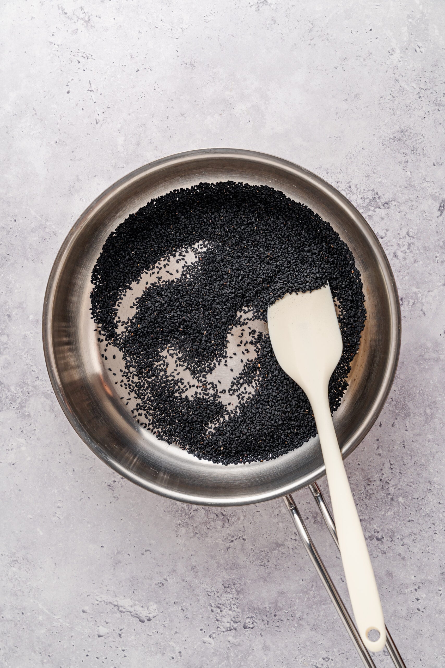 Toasting black sesame seeds - Catherine Zhang Black sesame seeds toasting in a dry stainless pan with a spatula