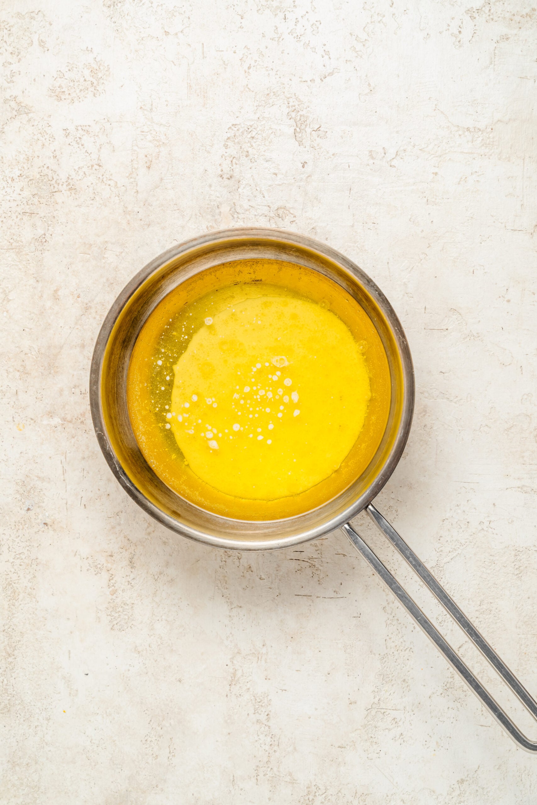 Melting butter for baklava - Catherine Zhang Melted butter in a steel saucepan with a layer of pale foam on the surface