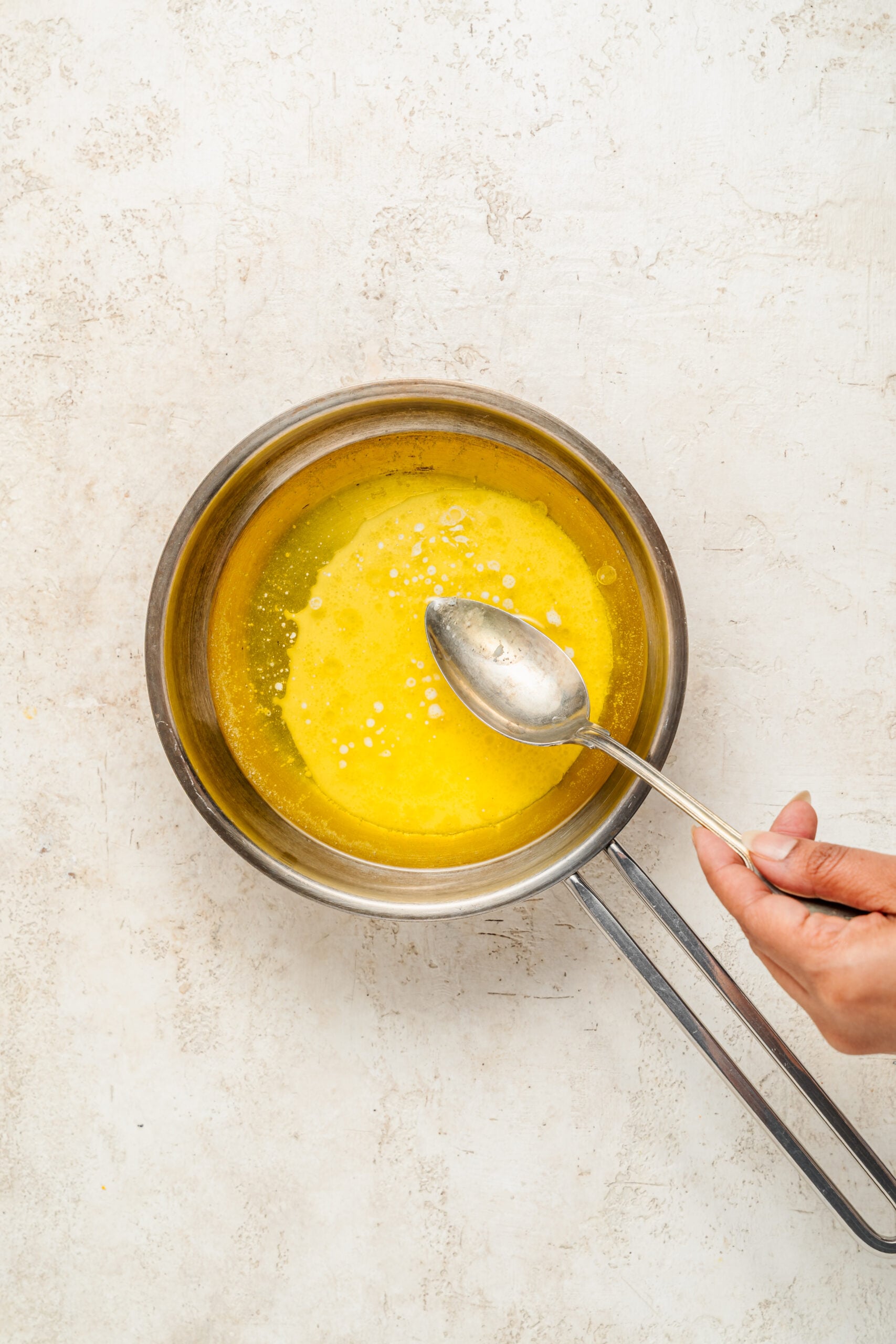 Skimming foam from clarified butter - Catherine Zhang A spoon skimming the foam off melted butter to clarify it for baklava