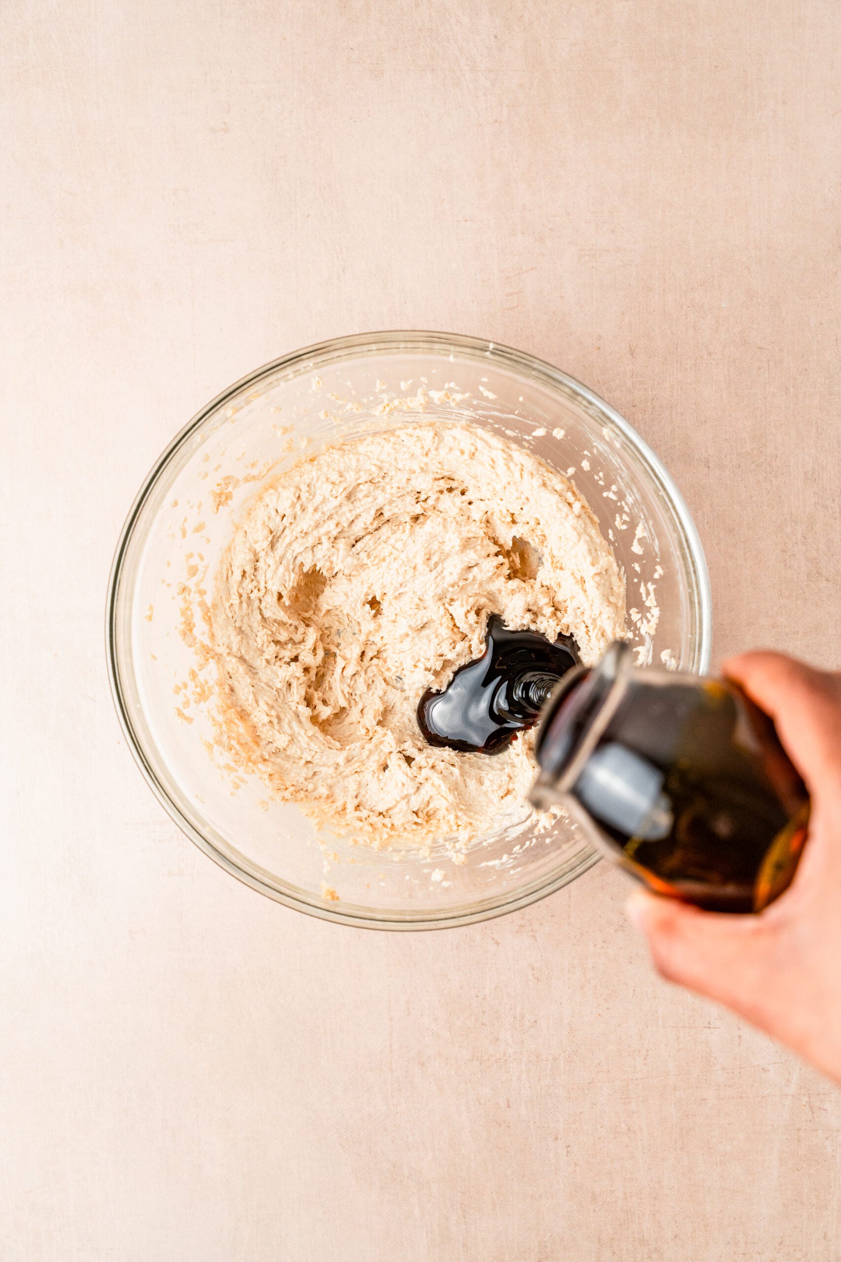 gingerbread-cookies-adding-molasses - Catherine Zhang Overhead shot of a glass mixing bowl with dough, as a hand pours a dark liquid from a bottle into it.