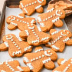 Decorated gingerbread cookies on a lined baking tray with a bowl of ground cinnamon