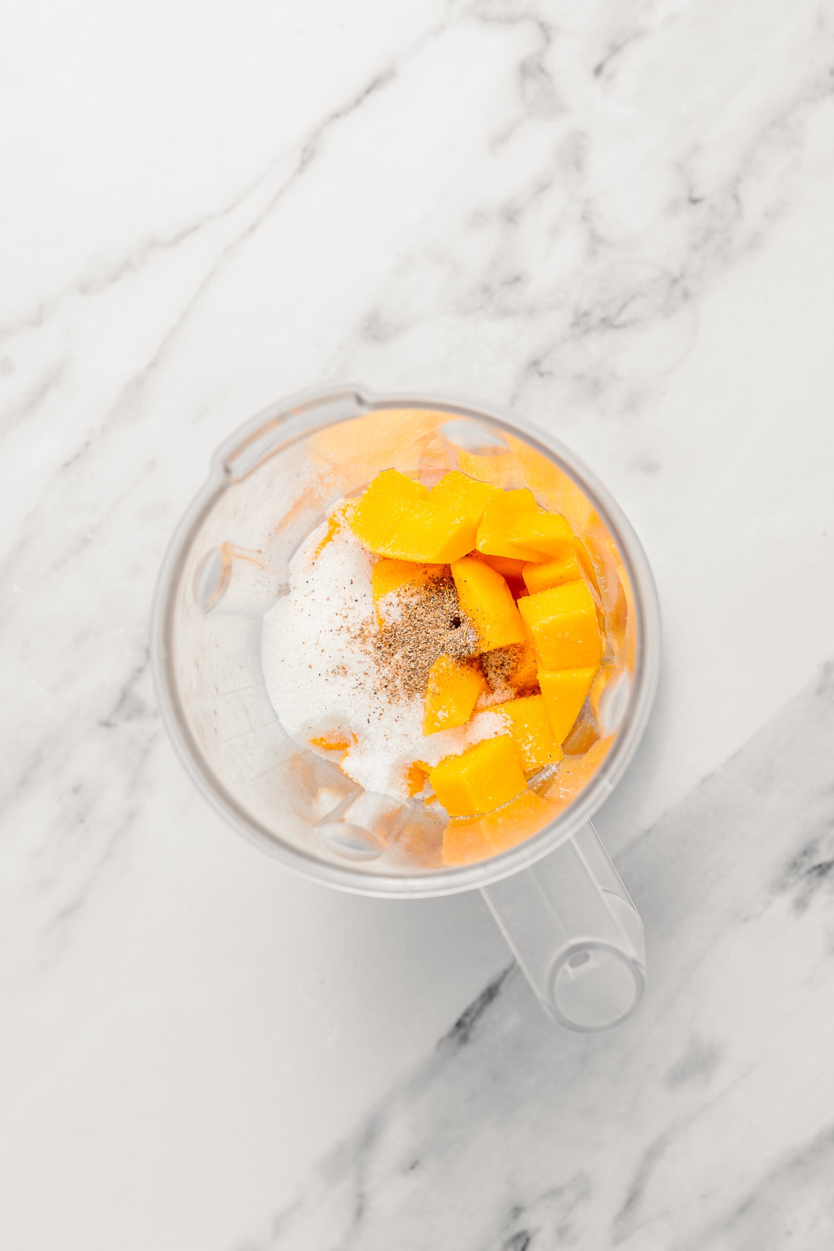 Mango, sugar and cardamom in the blender - Catherine Zhang Diced mango, sugar and ground cardamom in a blender jug before blending