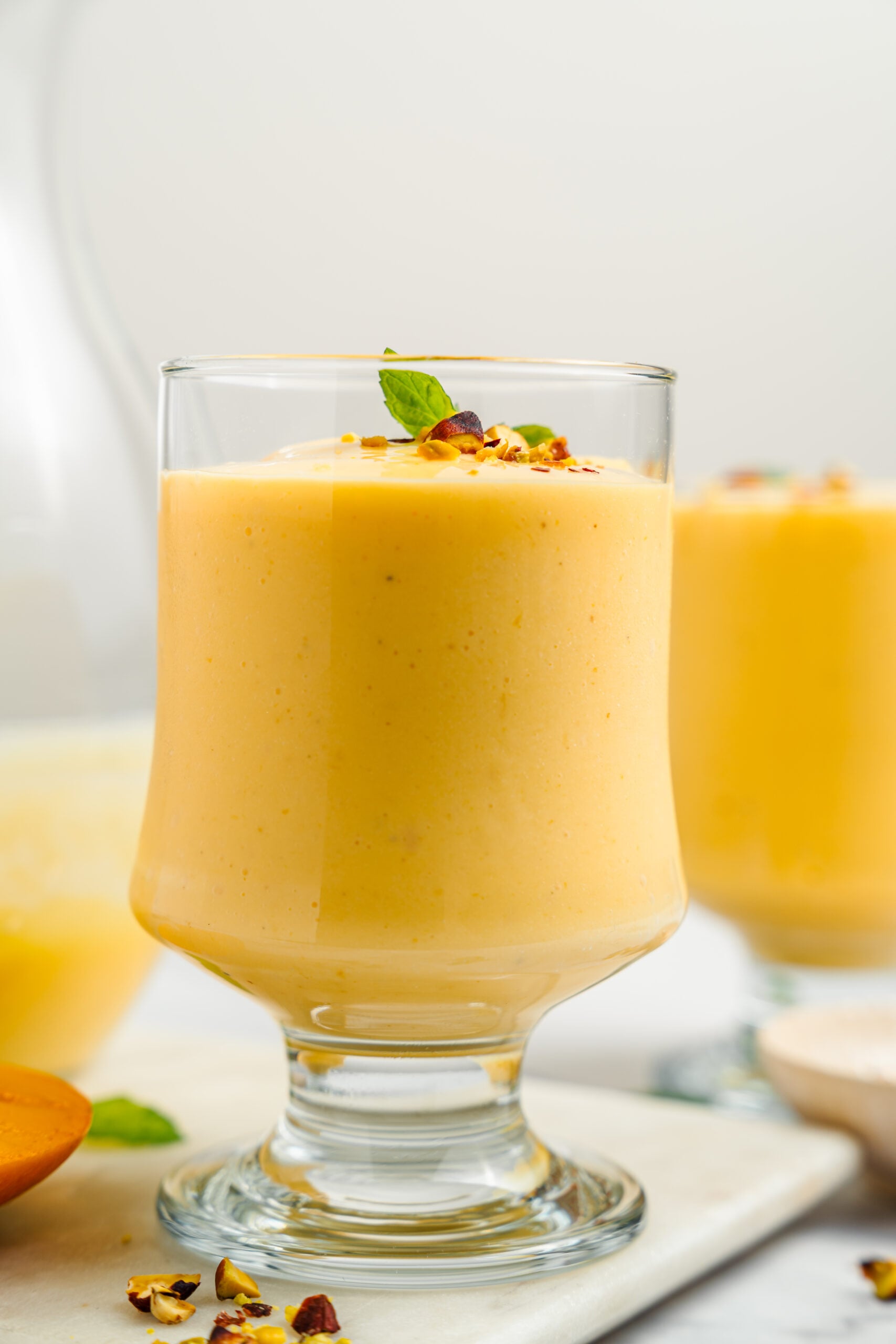 Mango lassi close up - Catherine Zhang Close up of a glass of mango lassi showing its thick, even, pale orange texture