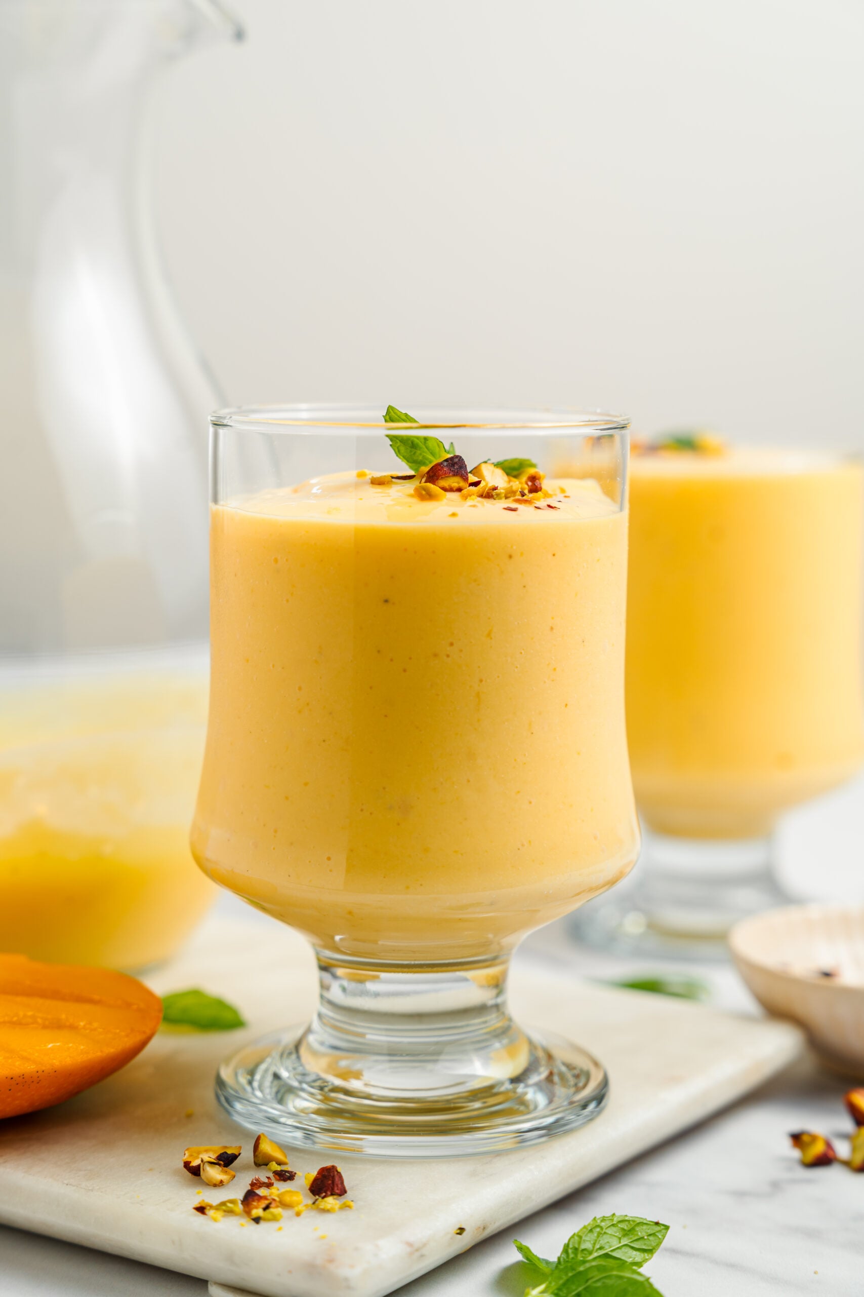 Styled glass of mango lassi - Catherine Zhang A styled glass of mango lassi with pistachios and mint beside fresh mango slices