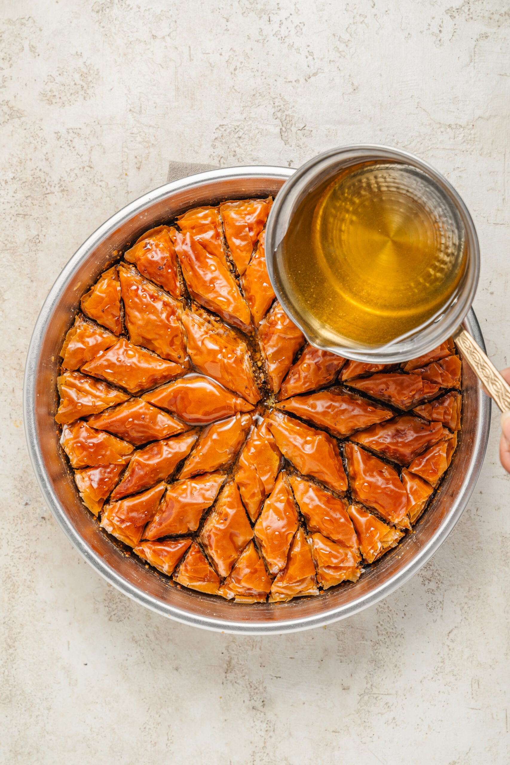 Pouring syrup over hot baklava - Catherine Zhang Cool honey lemon syrup poured from a small pan over the hot baked baklava
