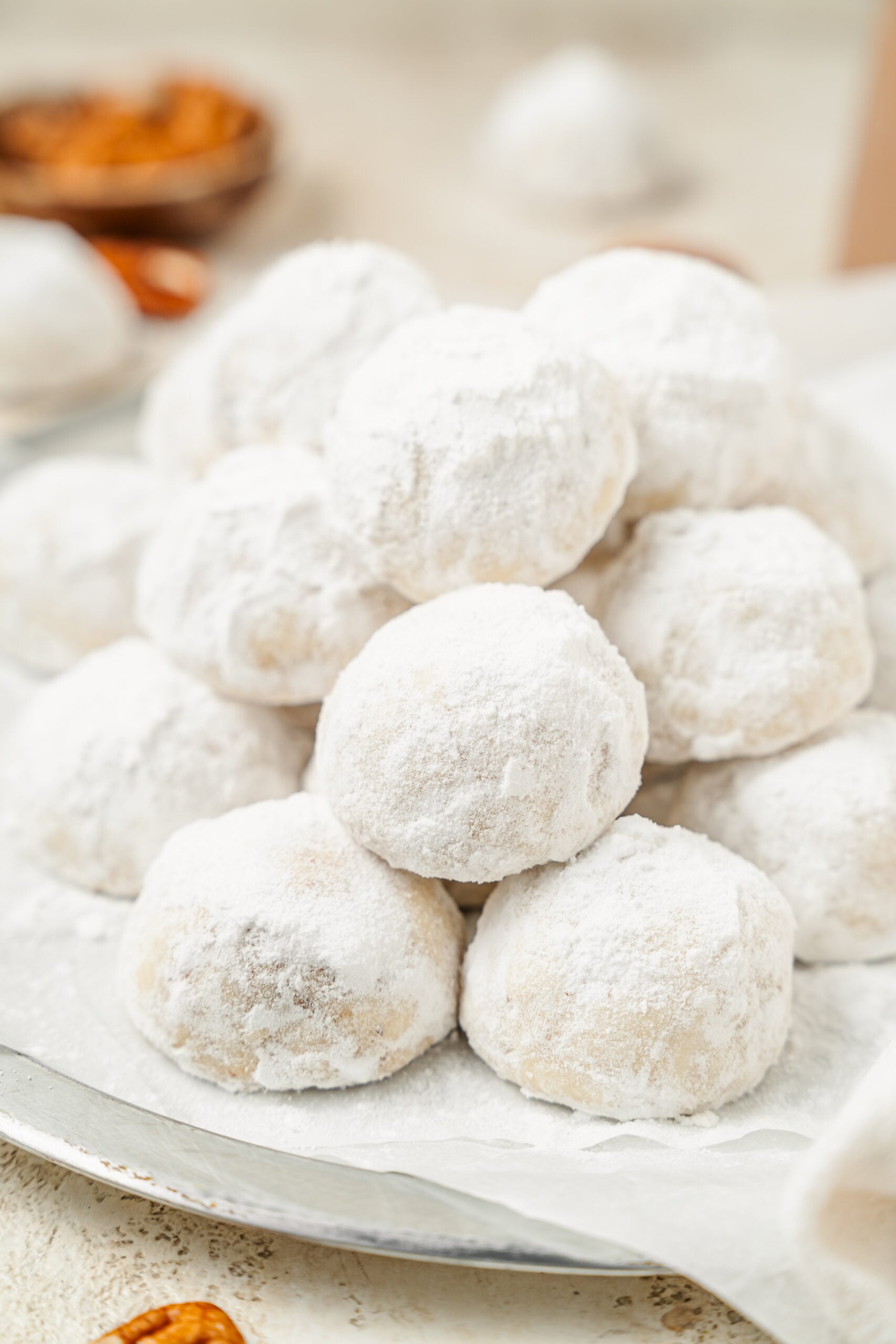 Snowball cookies on a plate with toasted pecans scattered around them - Catherine Zhang Snowball cookies on a plate with toasted pecans scattered around them